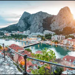 Widok na miasteczko Omiš w Chorwacji, z rzeką Cetiną i górami w tle. Słońce zachodzi nad malowniczą **Dalmacją**.