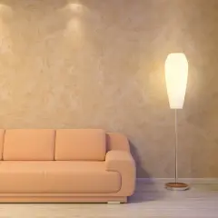 Miękka, brzoskwiniowa kanapa i elegancka lampa stojąca przy ścianie z fakturą przypominającą paca wenecka.