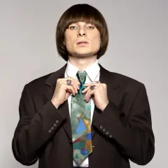 Ralph Kaminski w brązowej marynarce i kolorowym krawacie, poprawia węzeł.