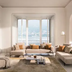 Un salon cocooning moderne avec canapé modulable, pouf, tapis et vue sur un lac.