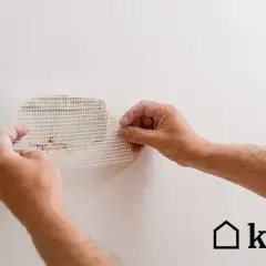 Ręce przykładają siatkę do dziur w ścianie. Świetny pomysł na zakrycie dziur w ścianie i naprawę ubytków.