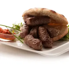 En tallrik med balkan mat: saftiga köttfärsrullar i pitabröd, serverade med en röd röra och grönsaker.