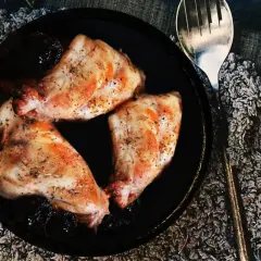 Trois morceaux de lapin aux pruneaux, assaisonnés et dorés, servis dans un plat noir avec une cuillère argentée.