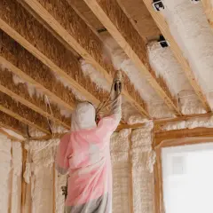 Persona con traje protector aplica espuma de poliuretano en el techo de una construcción.