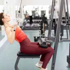 Kvinna tränar rygg med lat pull-maskin på gym.
