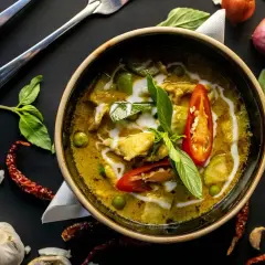 Aromatyczne curry z kurkumą, pełne zielonych warzyw i kawałków kurczaka, ozdobione chili i bazylią.