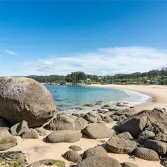 La **playa mourisca** se abre en una curva dorada bajo un cielo azul. Rocas gigantes y pequeñas salpican la arena y el agua turquesa.