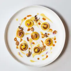 Piccolo capolavoro culinario: tartellette dorate con ripieno giallo, guarnite con calamari croccanti e fiori viola. Un'opera d'arte degna di un ristorante con massimo stelle Michelin.