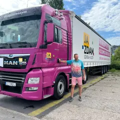 Mężczyzna obok różowej ciężarówki MAN, gotowy na zdobycie prawa jazdy kat C. Szkoła jazdy "Ja Zdam" zaprasza na kursy.