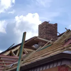 Budowa dachu z ceglanym kominem. Zastanawiasz się, czy komin można ocieplić styropianem? Na zdjęciu widać konstrukcję dachu i komin.