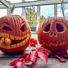Due zucche intagliate per Halloween, una con una bocca spalancata e un piccolo fantasma mandarino, circondate da foglie rosse. Idee zucche intagliate per un tocco spettrale.
