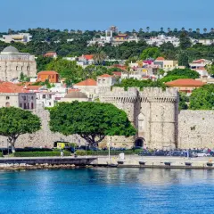 Kamienne mury obronne otaczają historyczne rodos miasto. W tle zielone wzgórza i białe budynki.