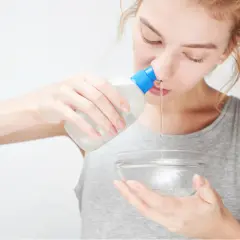Donna esegue lavaggi nasali con una bottiglietta e una ciotola.