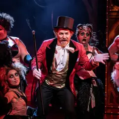 Scen från Moulin Rouge! The Musical i Stockholm. En cirkusdirektör med cylinderhatt och röd kavaj leder en färgstark ensemble.