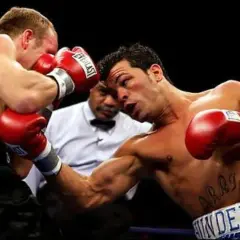 Boxer lands a powerful body shot, his opponent recoils as the referee watches closely.