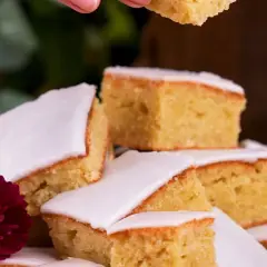En hög med bitar av saftig långpannekaka med glasyr, dekorerad med blommor. En bit lyfts upp.