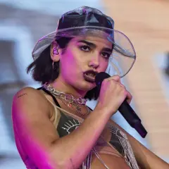 Dua Lipa w przezroczystym kapeluszu śpiewa do mikrofonu na koncercie.