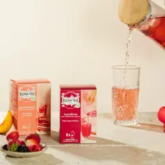 Kusmi Tea AquaRosa i AquaSummer w pudełkach, nalewanie różowej herbaty do szklanki. Obok owoce i hibiskus.