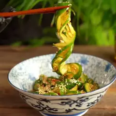 Chopsticks podnoszą zwinięty plasterek ogórka z miski pełnej tajskiej sałatki z ogórka, posypanej sezamem.