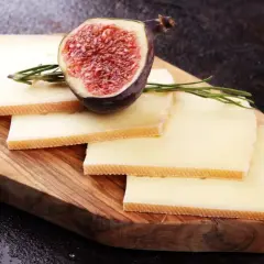 Tranches de fromage à raclette sur planche en bois, garnies d'une figue coupée et de romarin. Parfait pour une recette raclette 6 personnes.