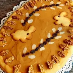 Okrągły mazurek kajmakowy z dżemem porzeczkowym, ozdobiony ciasteczkami zajączkami, orzechami i migdałami.