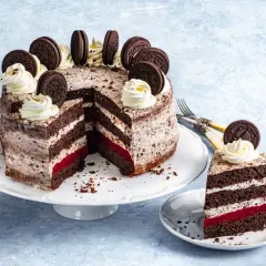Przepis na tort oreo: czekoladowe blaty, krem z ciasteczkami, malinowa warstwa i dekoracja z bitej śmietany i ciastek oreo.
