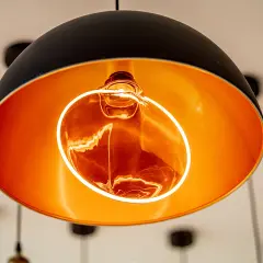 Lámpara colgante moderna con interior dorado y una bombilla decorativa Edison encendida, creando un ambiente cálido.