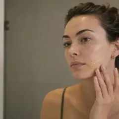 Kobieta aplikuje serum na twarz, zastanawiając się, czym są retinoidy i jak mogą poprawić jej cerę.