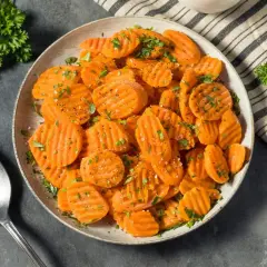 Carottes Vichy coupées en rondelles, saupoudrées d'herbes et de poivre, servies dans un plat avec une cuillère.