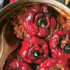 Röda, fyllda paprikor i en gryta med köttfärs och ris, redo att serveras med en träsked och en bit bröd.