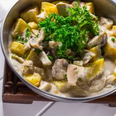 Pyszna potrawka z kurczaka z ziemniakami i pieczarkami w kremowym sosie, udekorowana natką pietruszki.