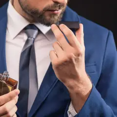 Elegancki mężczyzna w garniturze wącha perfumy, zastanawiając się, co mocniejsze: woda toaletowa czy perfumowana.