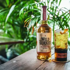 Un bicchiere di cocktail con bourbon Wild Turkey, ghiaccio e scorza d'arancia, accanto alla bottiglia.