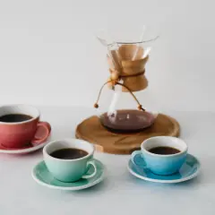 Chemex vs drip: trzy kolorowe filiżanki z kawą i szklany dzbanek Chemex na drewnianej podstawce.