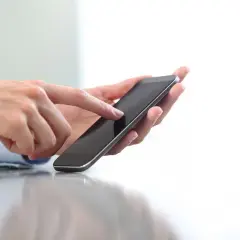 Dłonie trzymające smartfon, palec wskazujący dotyka ekranu. Szybko dowiesz się, jak doładować komuś konto ze swojego telefonu.