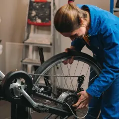 Kobieta w niebieskim kombinezonie reguluje łańcuch rowerowy.