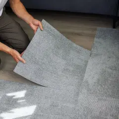 Pose d'une nouvelle moquette pour comment recouvrir un carrelage. Un homme pose une dalle de moquette grise sur un sol en bois.