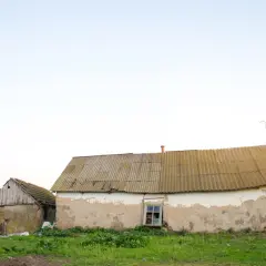 Dwa stare budynki gospodarcze, jeden z widocznym oknem, czekają na przekwalifikowanie na mieszkalne.