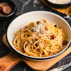 Ein Teller Spaghetti mit cremiger Sauce, garniert mit geriebenem Parmesan und schwarzen Pfefferkörnern. Darin versteckt sich leckerer Schinken für die perfekte Schinken Carbonara.