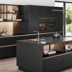 Cocina moderna con isla central, gabinetes negros, detalles dorados y electrodomésticos integrados.