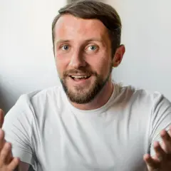 Mężczyzna z brodą i niebieskimi oczami, gestykulując, jakby zastanawiał się, czy mówienie do siebie jest normalne.