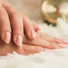 Mani curate con smalto rosa tenue su sfondo soffice. Scopri come idratare le unghie per una bellezza naturale.