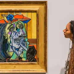 A woman gazes at a vibrant, cubist portrait, a striking example of obras de Pablo Picasso. The painting features a fragmented face with bold colors and sharp lines.