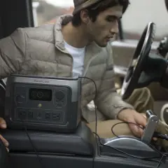 Un homme utilise une station d'énergie EcoFlow River 2 Max dans sa voiture. Avis sur la praticité en déplacement.