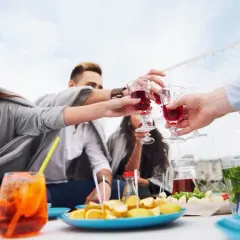 Grupa przyjaciół wznosi toast czerwonym napojem, ciesząc się aperitifem i przekąskami na świeżym powietrzu.