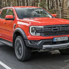 Pomarańczowy Ford Raptor jedzie po drodze w lesie. Sprawdź aktualną ford raptor cena i możliwości tego potężnego pickupa.