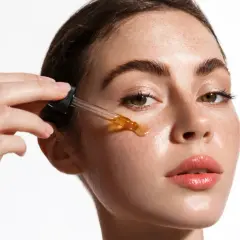Una mujer aplica un sérum con ácido salicílico y vitamina C en su rostro.