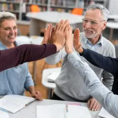 Lehrerteam gibt sich High-Five, um Burnout-Symptome zu bekämpfen. Freude und Zusammenhalt im Klassenzimmer.