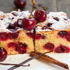 Dwa kawałki ciasta z czereśniami, posypane cukrem pudrem, ozdobione świeżymi owocami i laskami wanilii.