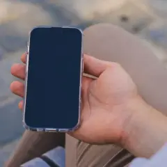 Mężczyzna trzyma iPhone'a w przezroczystym etui. Zastanawia się, jak wyłączyć iPhone'a, aby oszczędzić baterię.